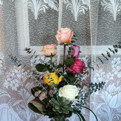 Mixed roses in a clear glass vase with eucalyptus and decorative foliage