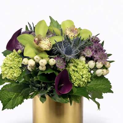 Mixed floral arrangement in a gold cylinder vase with green orchids and purple blooms