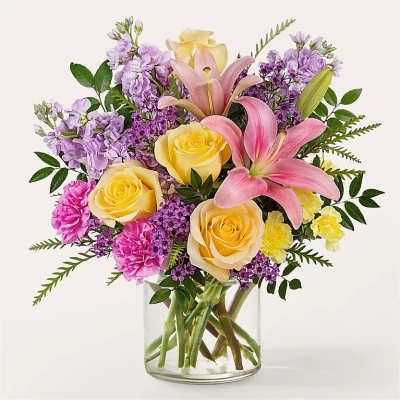Bouquet of pink lilies, yellow roses, and purple flowers in a clear glass vase