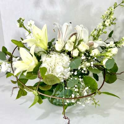 White lilies and roses arranged in a glass vase with greenery