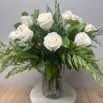 White roses arranged in a clear glass vase with green foliage