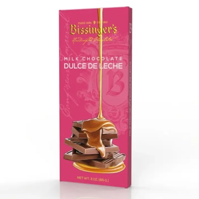 Pink boxed milk chocolate dulce de leche bar with caramel pouring over stacked chocolate pieces