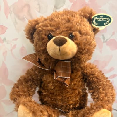 Brown teddy bear with a plaid bow tie against a floral background