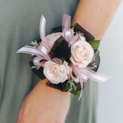 Blush rose wrist corsage with pink and black ribbon on a person’s arm