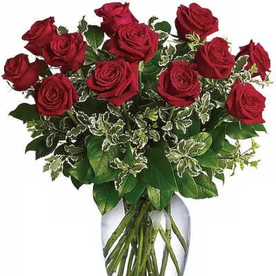 Red roses arranged in a clear glass vase with variegated greenery