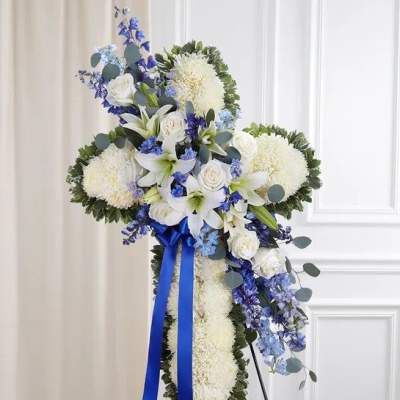 Standing cross-shaped spray of white mums with white lilies, roses, blue flowers, and a blue ribbon.