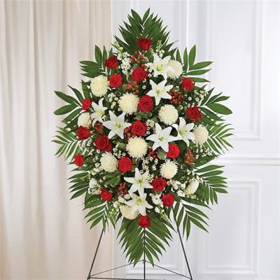 Tall standing spray of red roses, white lilies, and white mums on a metal easel.