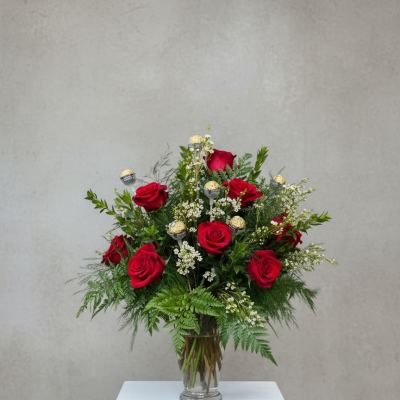 Red roses arranged in a clear glass vase with greenery and small white filler flowers