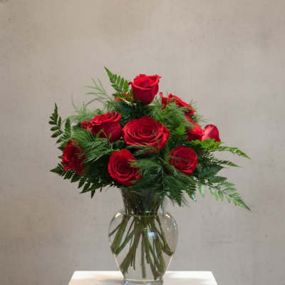Red roses arranged in a clear glass vase with greenery
