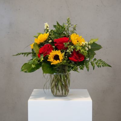 Bouquet of red roses and yellow sunflowers in a clear glass vase