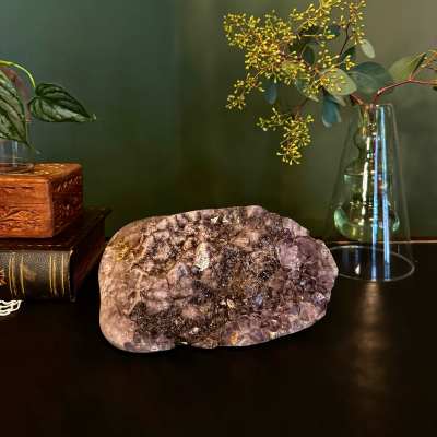 Amethyst crystal cluster on a dark surface beside a glass vase with branches