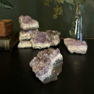Purple crystal clusters on a dark surface with a glass vase of stems in the background