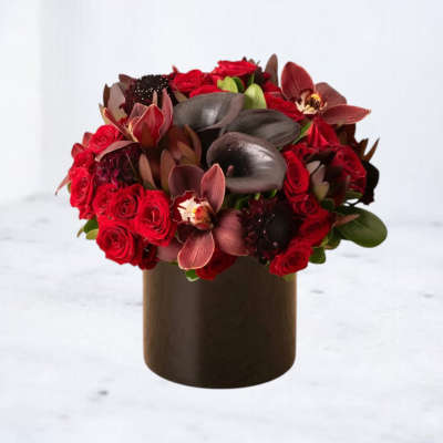 Low red rose and dark calla lily arrangement with orchids in a round black vase