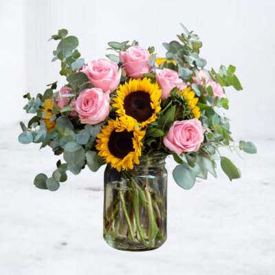 Medium bouquet of pink roses and bright sunflowers in a clear glass jar vase with eucalyptus.
