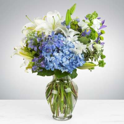 Bouquet of white lilies and blue hydrangeas in a clear glass vase
