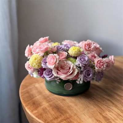 Round arrangement of pink and lavender roses in a green box