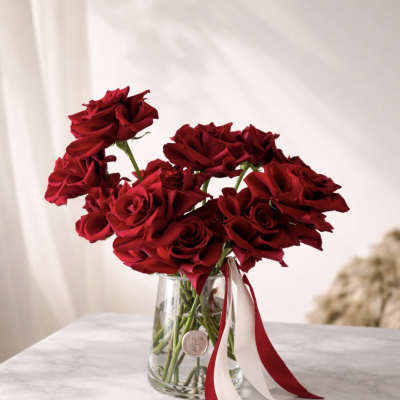 Red roses in a clear glass vase with red and white ribbons
