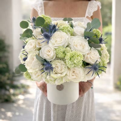 White rose bouquet with pale green hydrangeas and blue thistle in a white hatbox