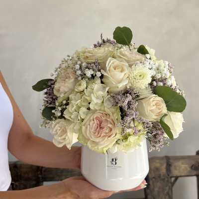 Cream roses and hydrangeas in a white vase with green leaves