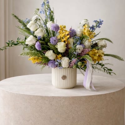 Mixed bouquet of white, yellow, and lavender flowers in a ribbed vase