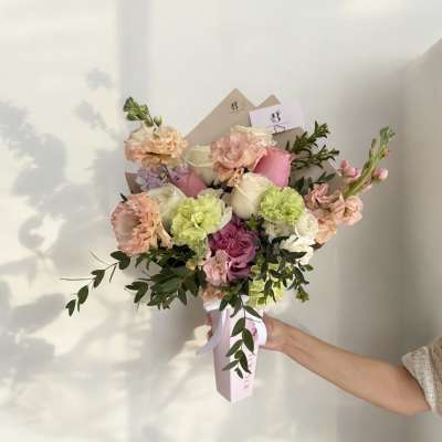 Handheld bouquet of pink, white, and peach flowers with greenery