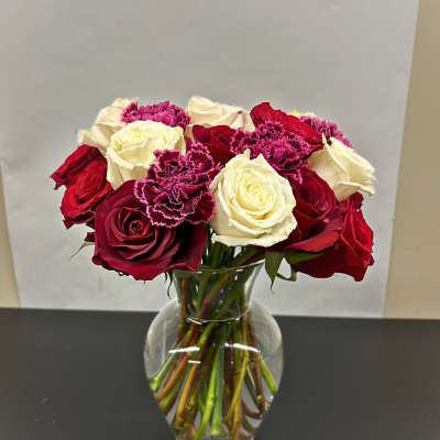 Bouquet of red and white roses with magenta carnations in a clear glass vase.