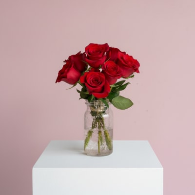 Red roses in a clear glass jar vase on a white pedestal