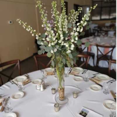 Tall white floral centerpiece in a clear glass vase on a round table
