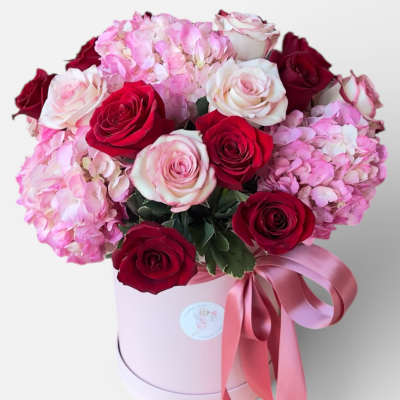 Pink and red roses with hydrangeas in a round pink box tied with ribbon