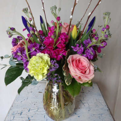 Mixed bouquet of pink roses, purple blooms, and pussy willow in a glass vase