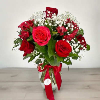 Red roses and baby's breath in a glass vase with a red ribbon