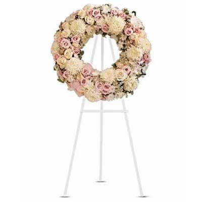 Round floral wreath on a white easel with pale pink and cream flowers