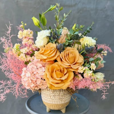 Peach roses and pale pink flowers in a cream vase with pink filler