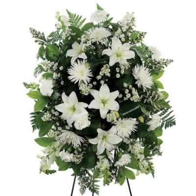 Standing spray of white lilies, carnations, and mums with small white fillers and lush greenery on an easel.
