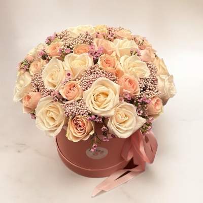 Cream and blush roses arranged in a pink round box with a ribbon