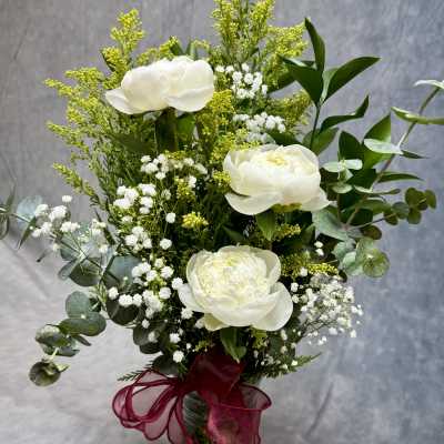 White peonies in a glass vase with baby's breath and greenery
