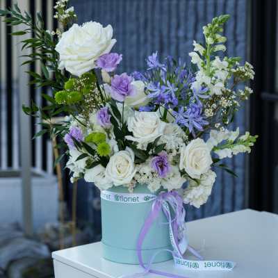 White and lavender floral arrangement in a pale blue hatbox