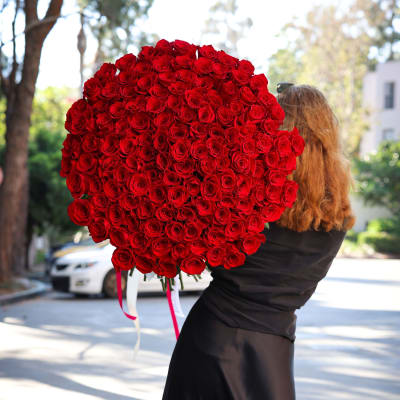 Large bouquet of red roses held by a woman outdoors