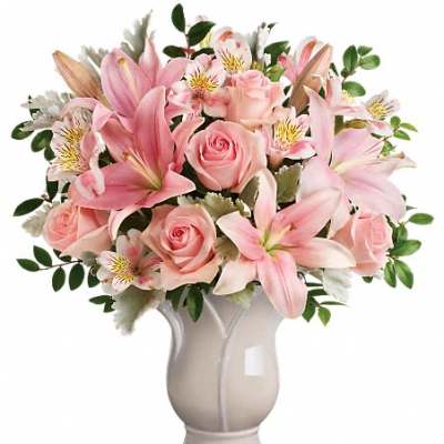 Pink lilies, roses, and alstroemeria arranged in a pale ceramic urn-shaped vase