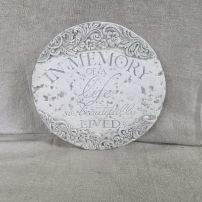 Round stone memorial plaque with carved floral border and inscription