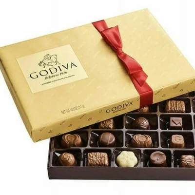 Gold box of assorted chocolates with red ribbon, lid partly open to show filled tray