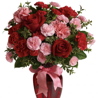 Red roses and pink carnations in a red glass vase with a pink ribbon