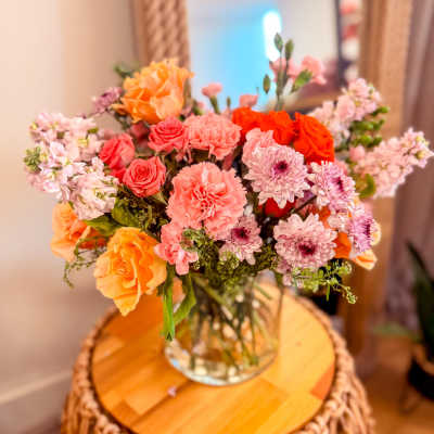 Bouquet of orange, pink, and lavender flowers in a clear glass vase