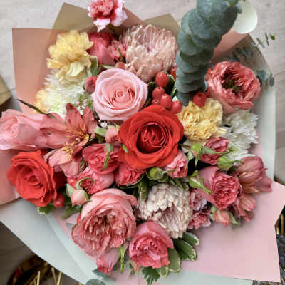Bouquet of pink and red roses with mixed blooms wrapped in pastel paper