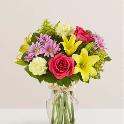 Mixed bouquet of roses, lilies, daisies, and carnations in a glass vase