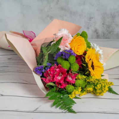 Mixed bouquet with sunflowers, roses, carnations, and alstroemeria in pastel wrap