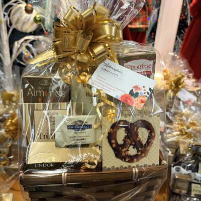 Gift basket of assorted chocolates and treats wrapped in cellophane with a large gold bow