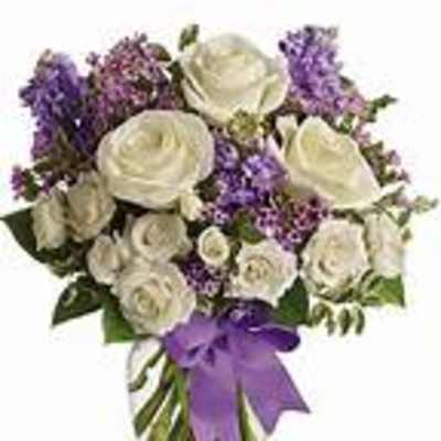 White roses and purple flowers in a clear vase with a purple ribbon