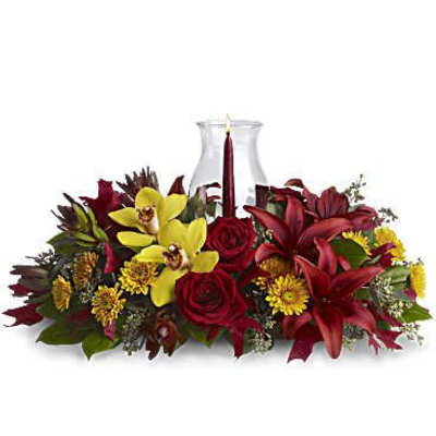 Red roses and yellow orchids arranged around a glass vase with a candle