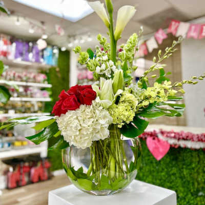 Low glass bowl of red roses, white hydrangeas, calla lilies and green blooms in an asymmetrical arrangement